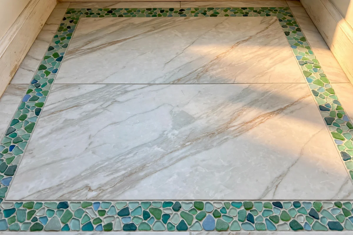 Marble effect floor tiles with sea glass mosaic border in an elegant bathroom