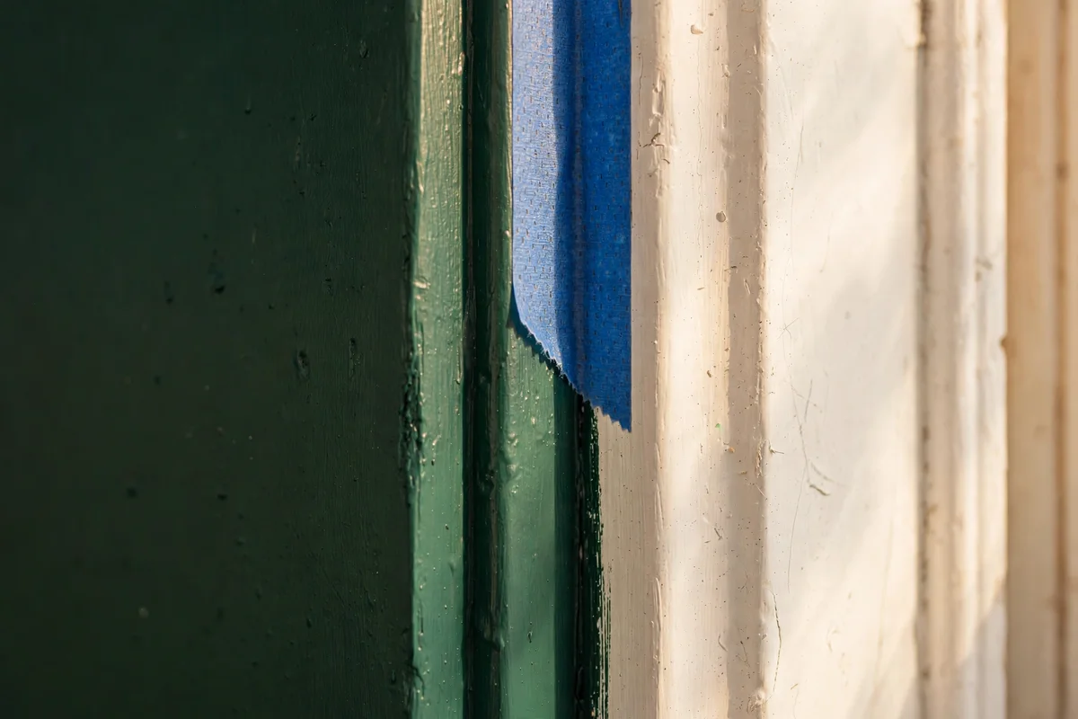 A close view of a painted door edge with crisp tape lines, dark green against a white frame