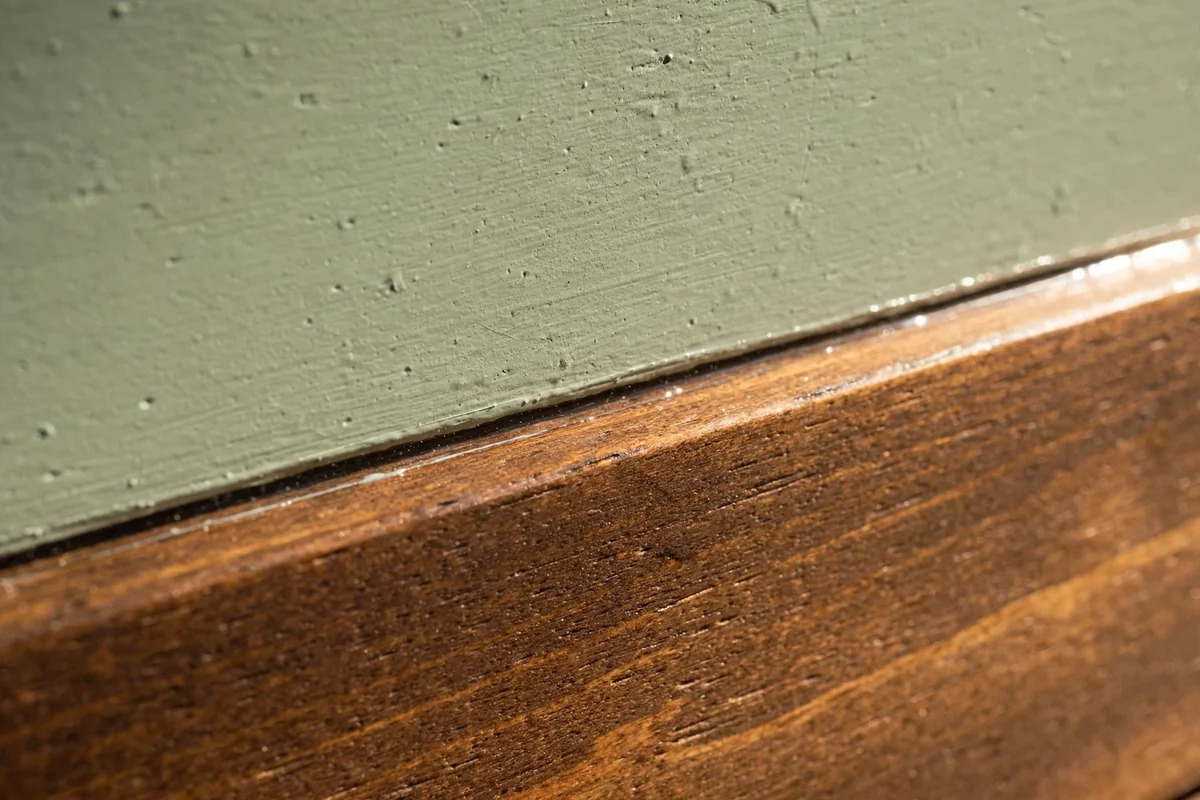 Close view of the crisp border where sage paint meets stained wood, sealed with clear topcoat